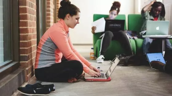 woman sitting on floor with laptop and 2 others on chairs
